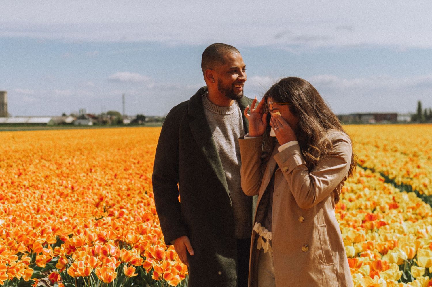 A woman wipes away tears after a secret proposal moment – tulip fields in the background.