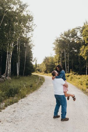 Couple shares romantic moment on tree-lined gravel path.