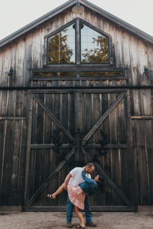Couple poses playfully in front of rustic wooden barn.