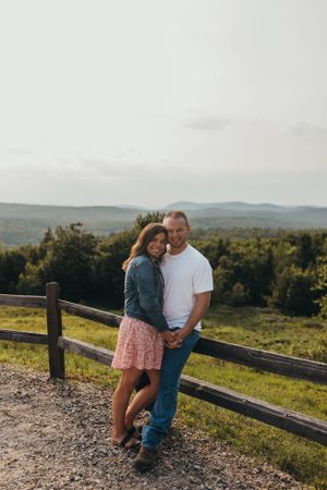 Couple shares intimate moment against wooden fence with mountain vista.