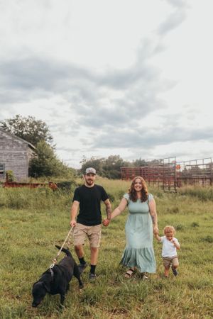 Family and dog posing in a grassy field with farm equipment in the background.