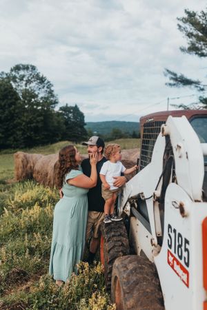 Family sharing intimate moments near vintage farm equipment in a field.