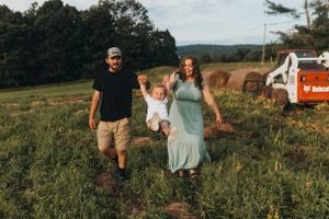 Family playfully swings child in field during golden hour sunset.