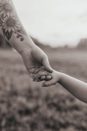 Black and white close-up of hands with floral tattoo reaching across a field.