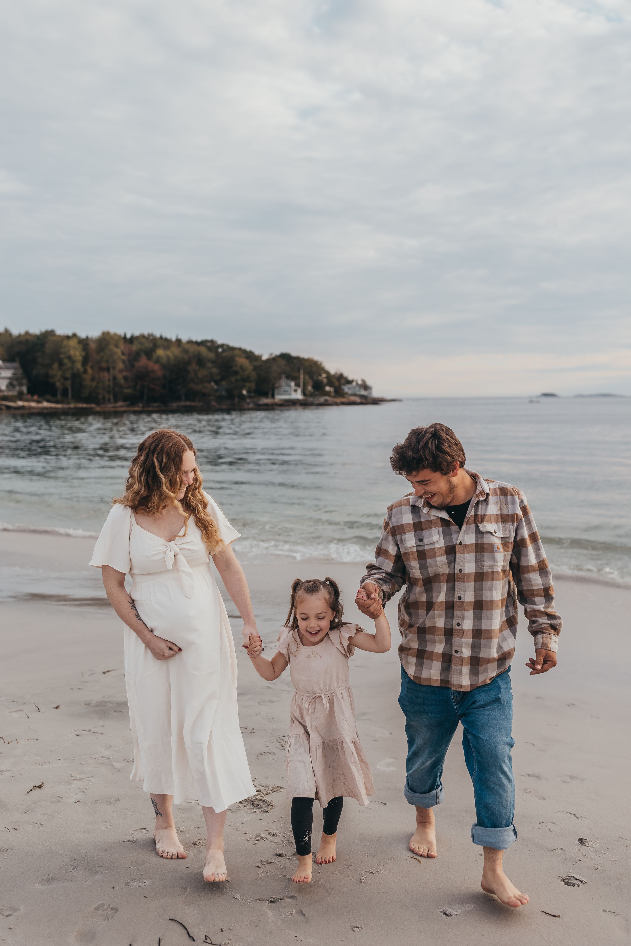 A family walks together barefoot along a sandy beach during a cloudy day.
