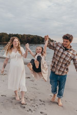 People holding hands and laughing while walking on a beach during an overcast day.