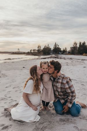A sweet family moment captured while sitting together on a sandy beach at sunset.