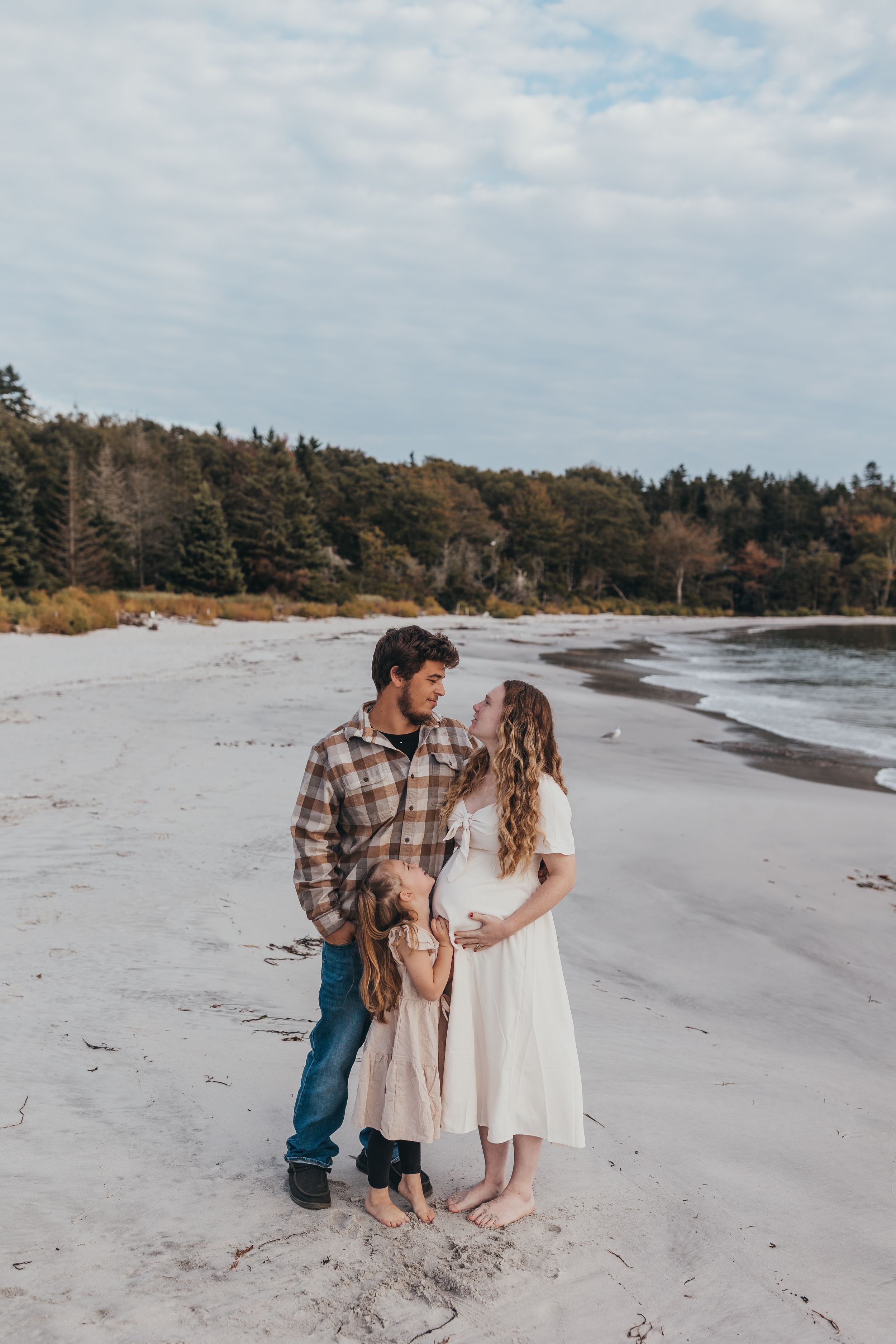 Family portrait session on sandy beach with pine trees in background.