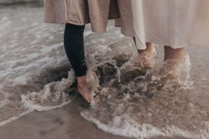 Bare feet walking through gentle ocean waves on a sandy shore.