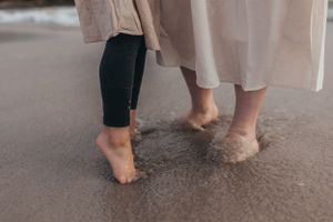 Close-up of bare feet walking through shallow ocean water on wet sand.