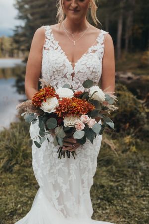 Bride holds stunning autumn bouquet with white and rust colored flowers.