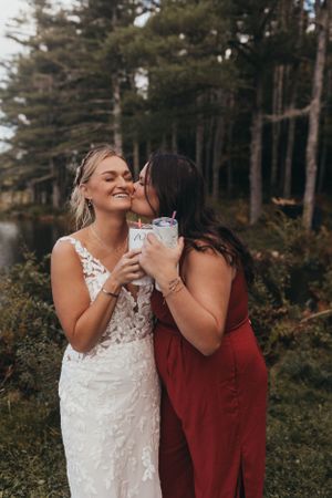 Two people in wedding attire sharing drinks and laughing together outdoors.