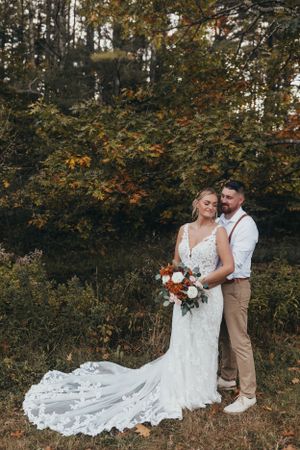 A couple poses for romantic wedding photos in a natural outdoor setting with fall foliage.