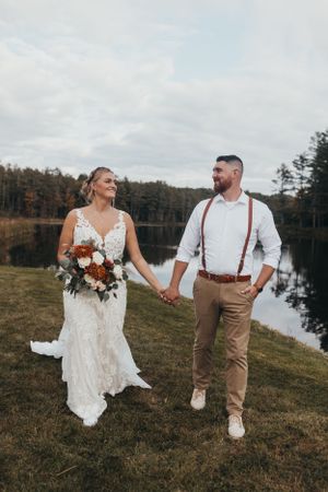 Newlyweds walk hand in hand along a lakeside path during their autumn wedding.