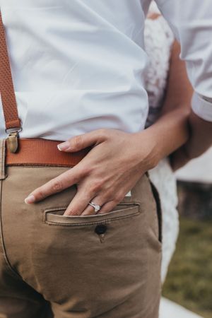 Close-up detail shot of khaki pants with leather suspenders and wedding ring.