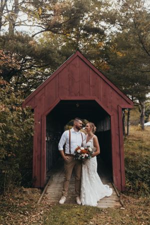 Wedding couple poses together inside a rustic red covered bridge.