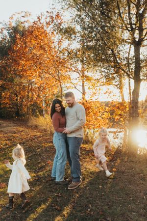 Family enjoying playful moments together on a hillside during an autumn sunset photoshoot.