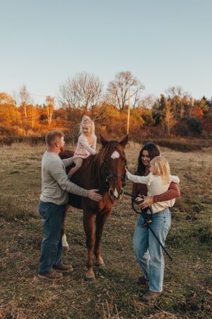 Family interacting with a brown horse in a field during a fall photography session.