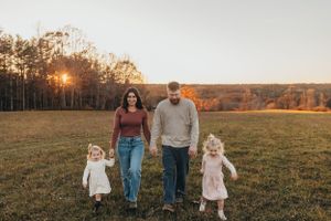 Family walking together through a sunlit meadow during sunset.