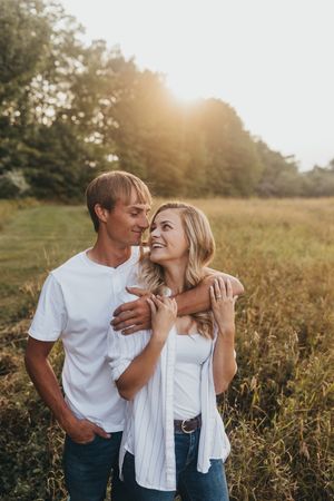 Couple embracing in sunlit meadow during golden hour.