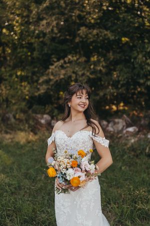 Bride holding colorful autumn bouquet with orange and white flowers in outdoor setting.