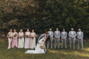 Wedding party poses outdoors in formal attire with bridesmaids in pink dresses and groomsmen in gray suits.