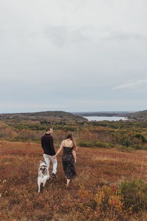 Couple walking with dog through autumn landscape overlooking lake vista.