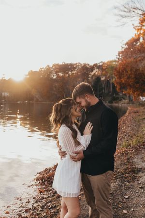 Romantic lakeside moment at sunset with fall foliage in background.