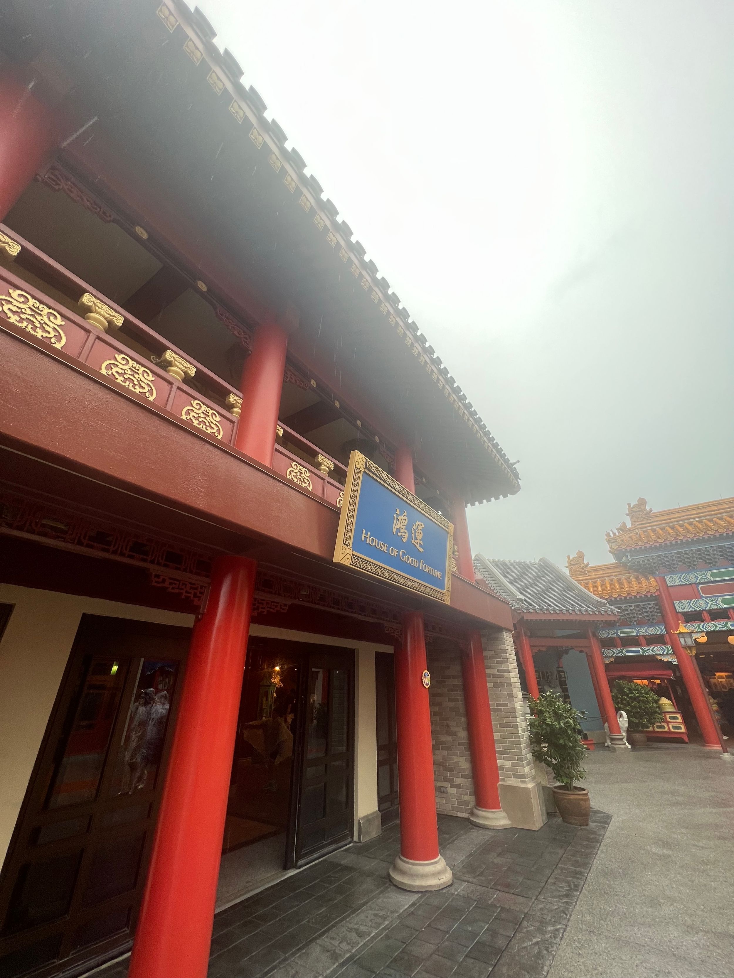 Traditional Chinese temple exterior with red pillars and ornate architectural details on a cloudy day.