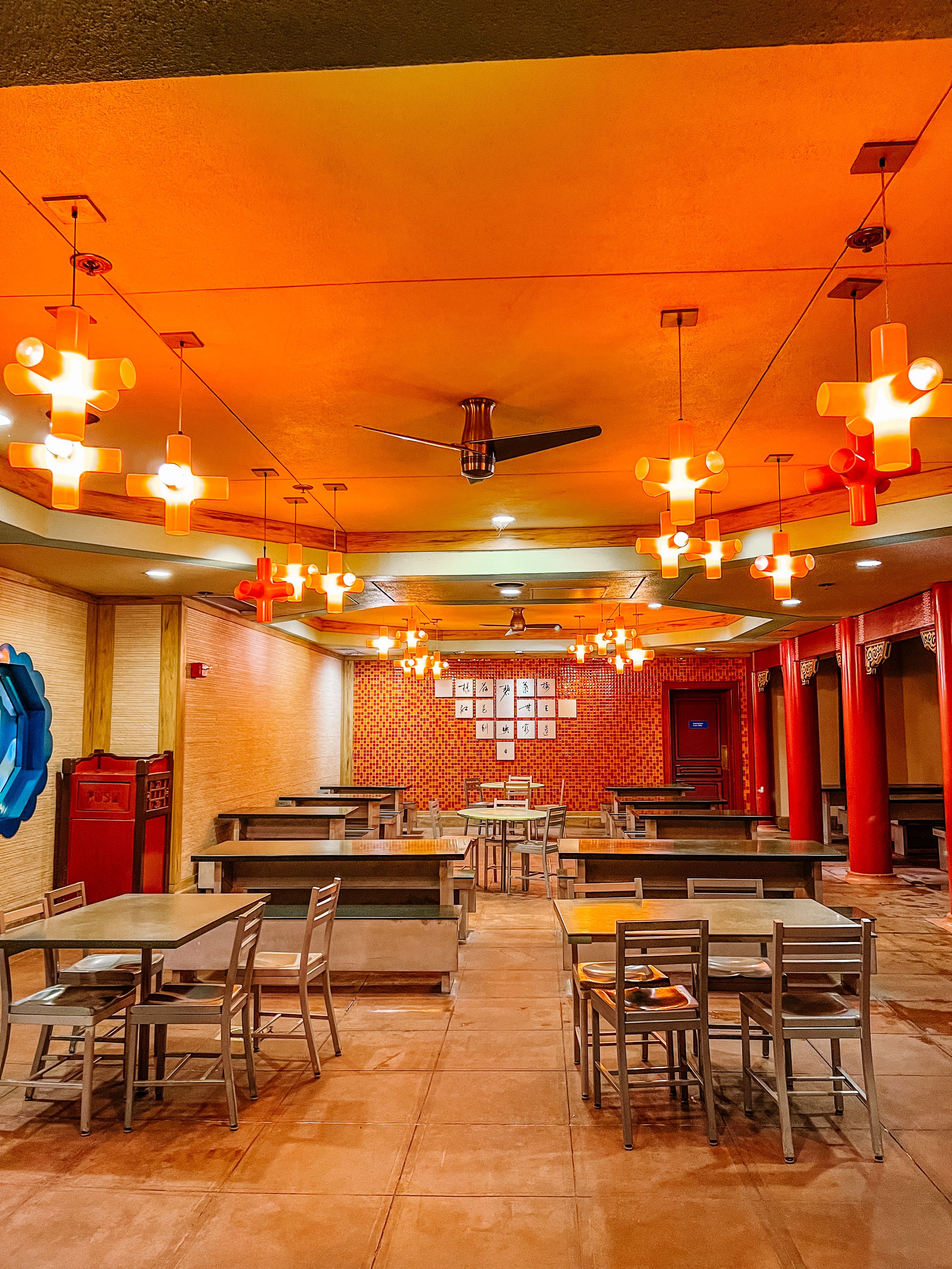 Modern Chinese restaurant interior with warm lighting, red columns and empty tables.