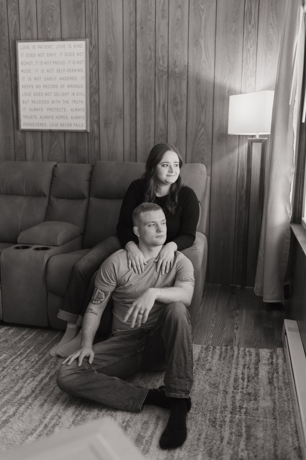 A cozy indoor portrait session featuring a couple on a gray sofa against wood paneling.