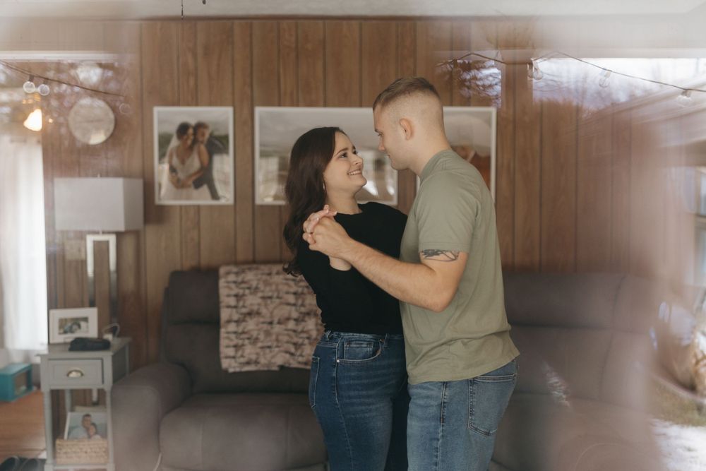Couple dancing together in living room with wood paneled walls and vintage decor.