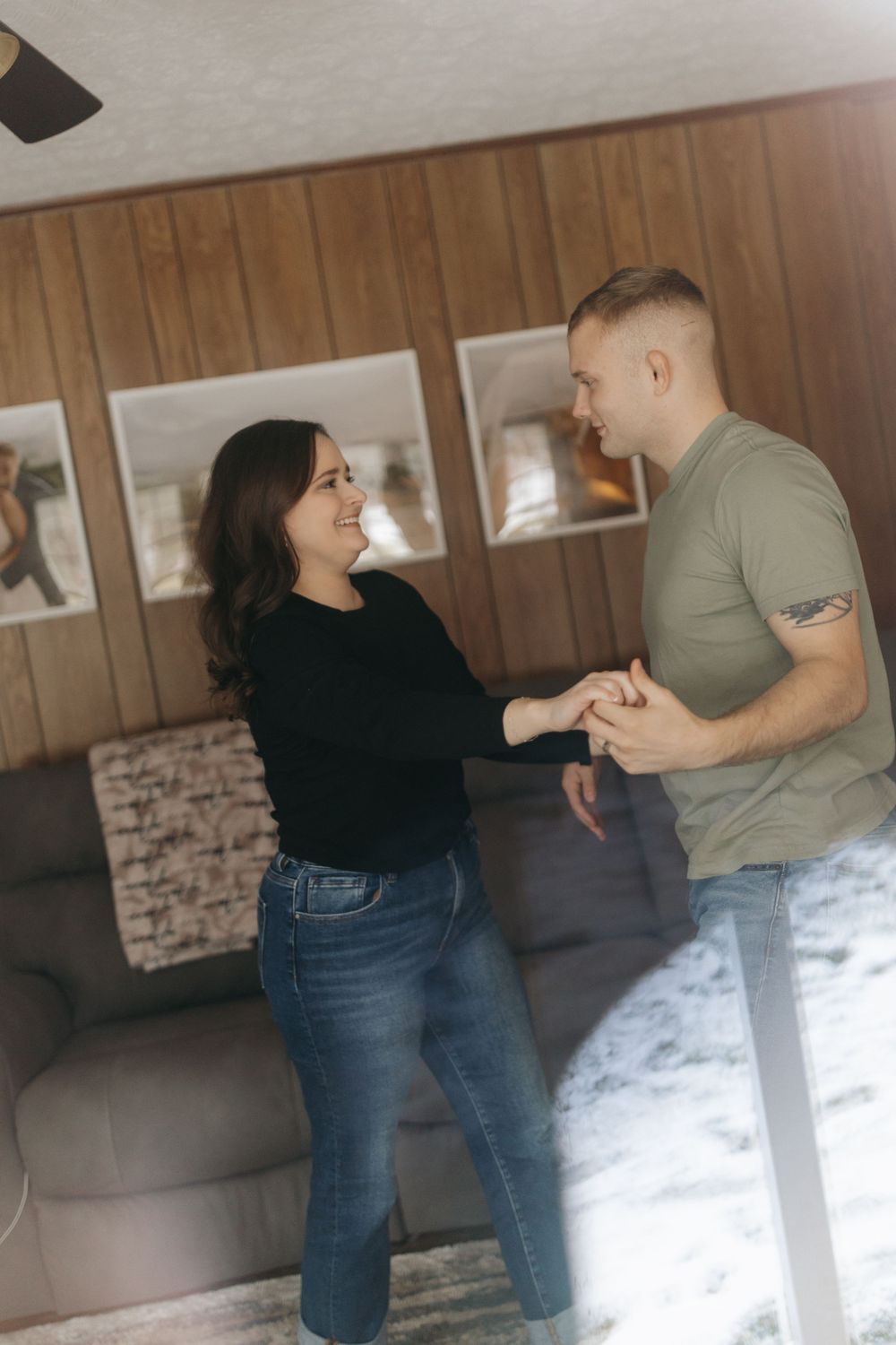Playful dancing scene with couple in casual outfits against wood paneled wall.