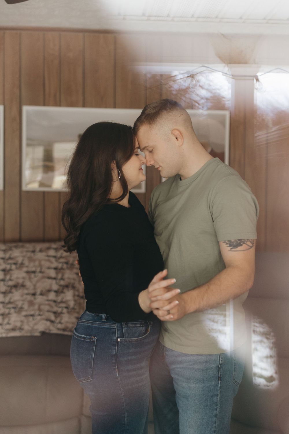 Intimate portrait of couple embracing in living room with wood paneling.
