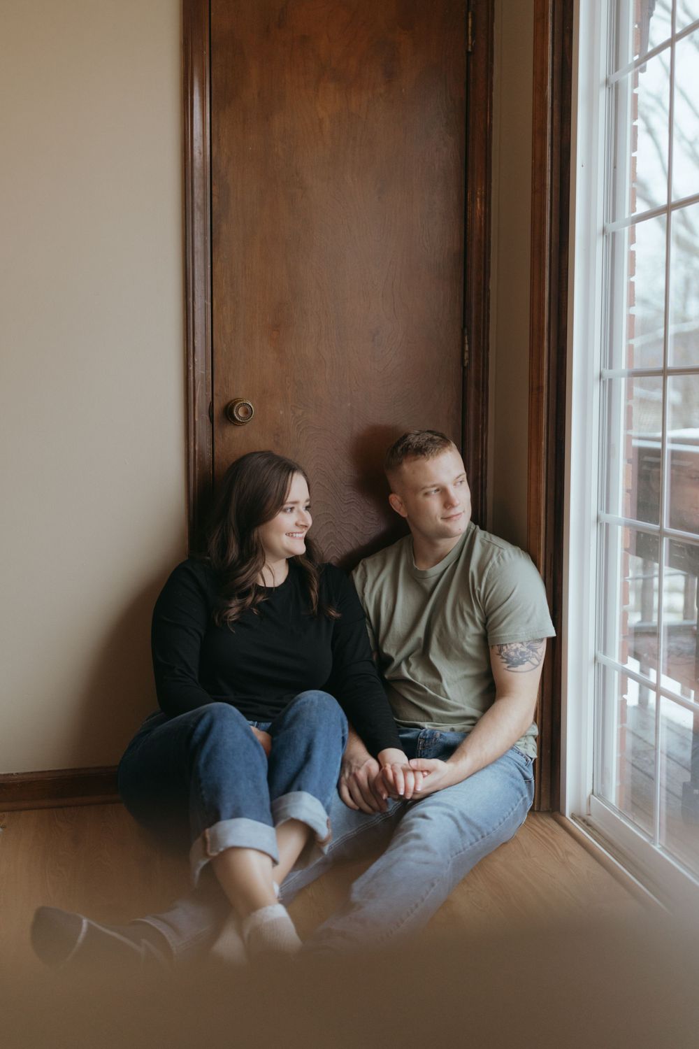 Couple sitting by window in casual clothes sharing tender moment together.