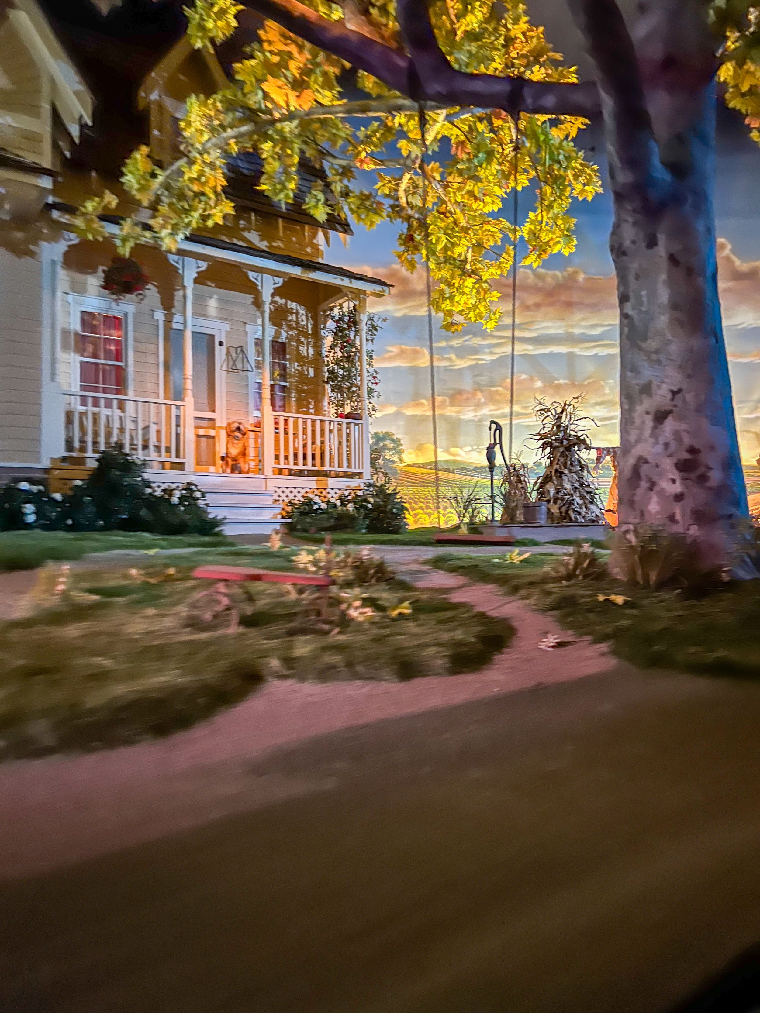A cozy front porch with autumn yellow leaves and a stunning sunset glowing through the trees in the background.