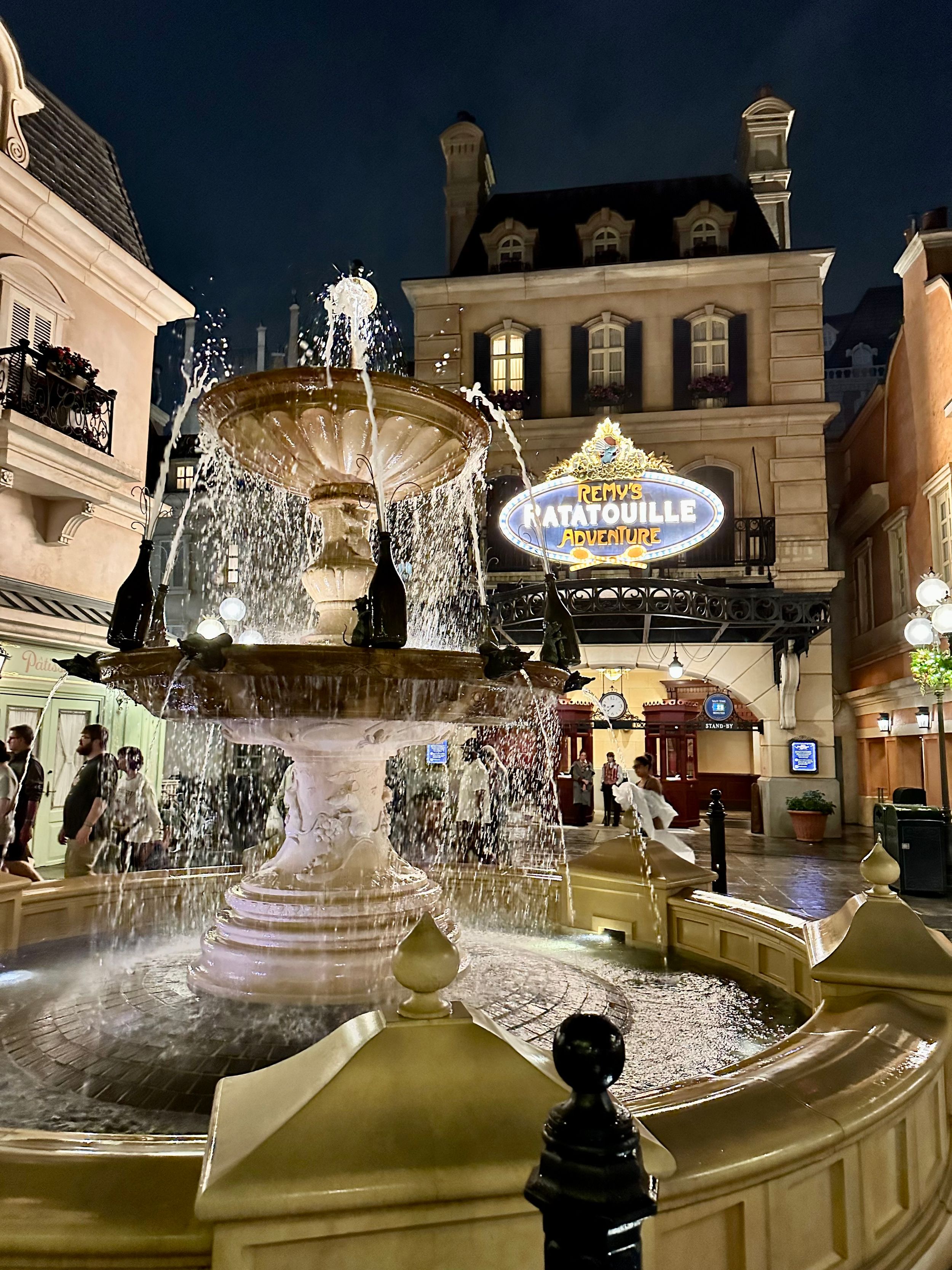 Ornate fountain illuminated at night in front of Ratatouille restaurant with classic French architecture in EPCOT theme park.