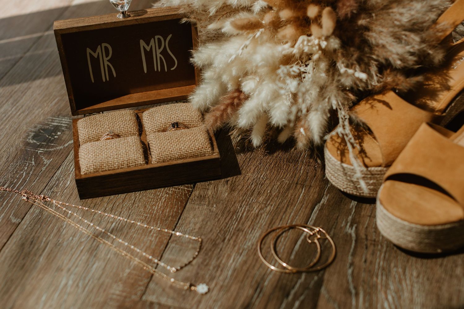 Wedding details including rings, Mr & Mrs sign, and rustic decor arranged on wooden surfaces.