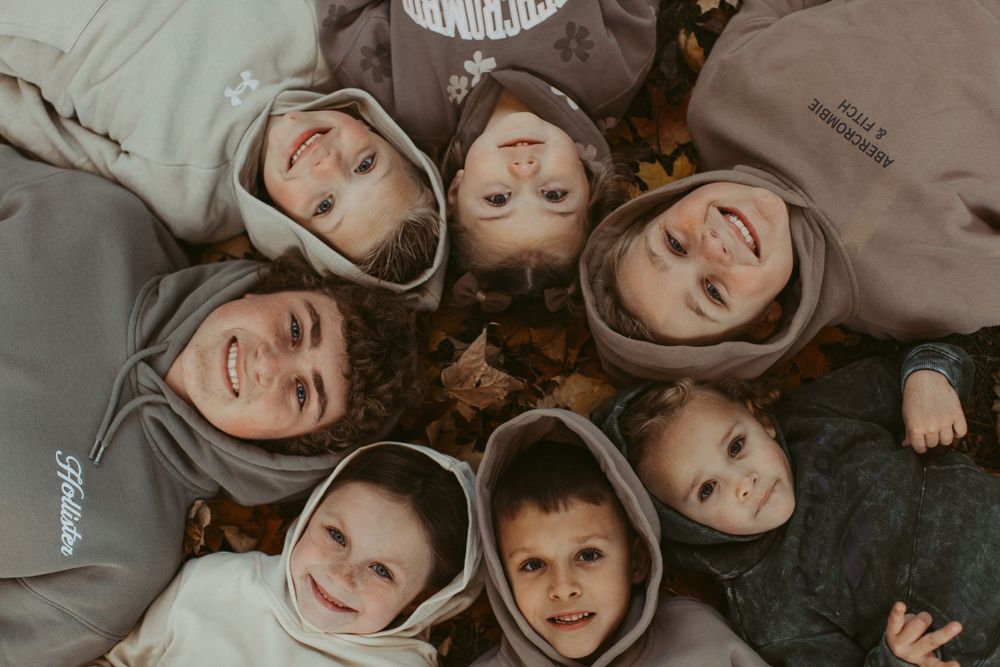 People lying on ground wearing matching hooded sweatshirts in playful pose.