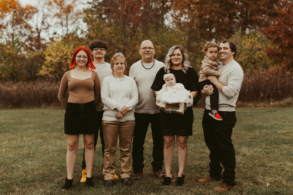 Extended family members pose together on a grassy hill during fall season.