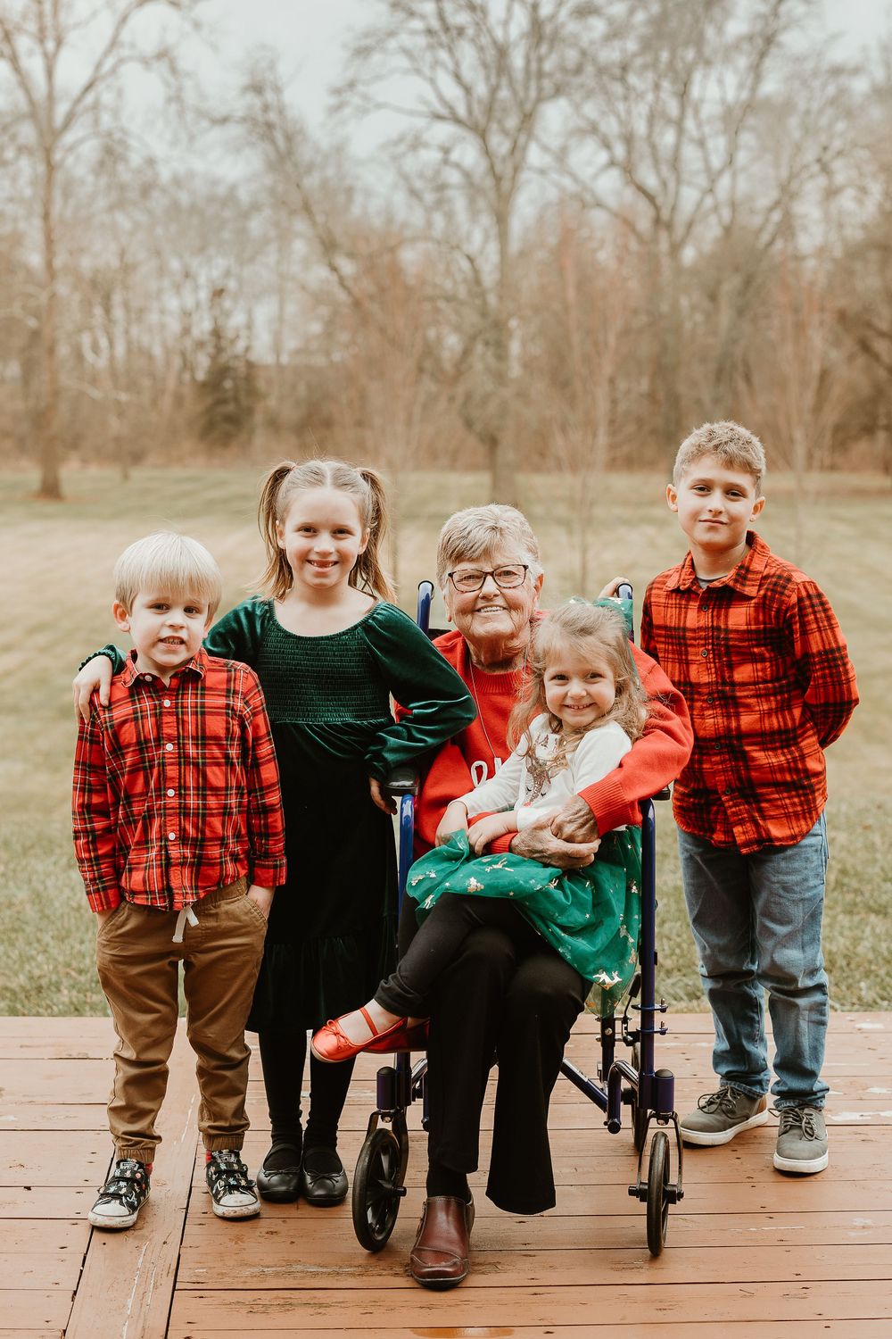 A group of children in plaid and dark clothing sit together on a wooden deck in an autumn setting.