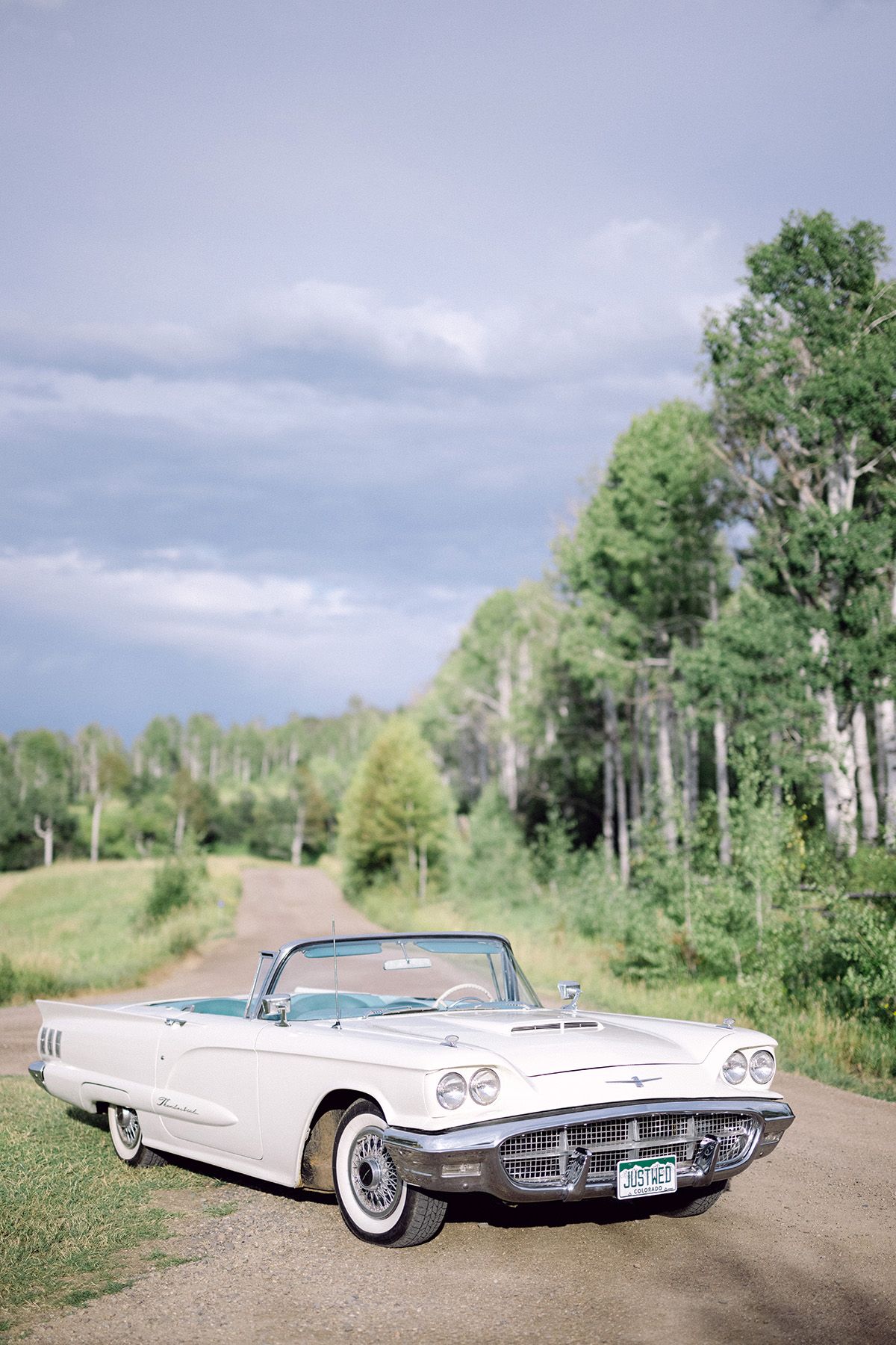 Classic white 1950s Thunderbird convertible on mountain dirt road.