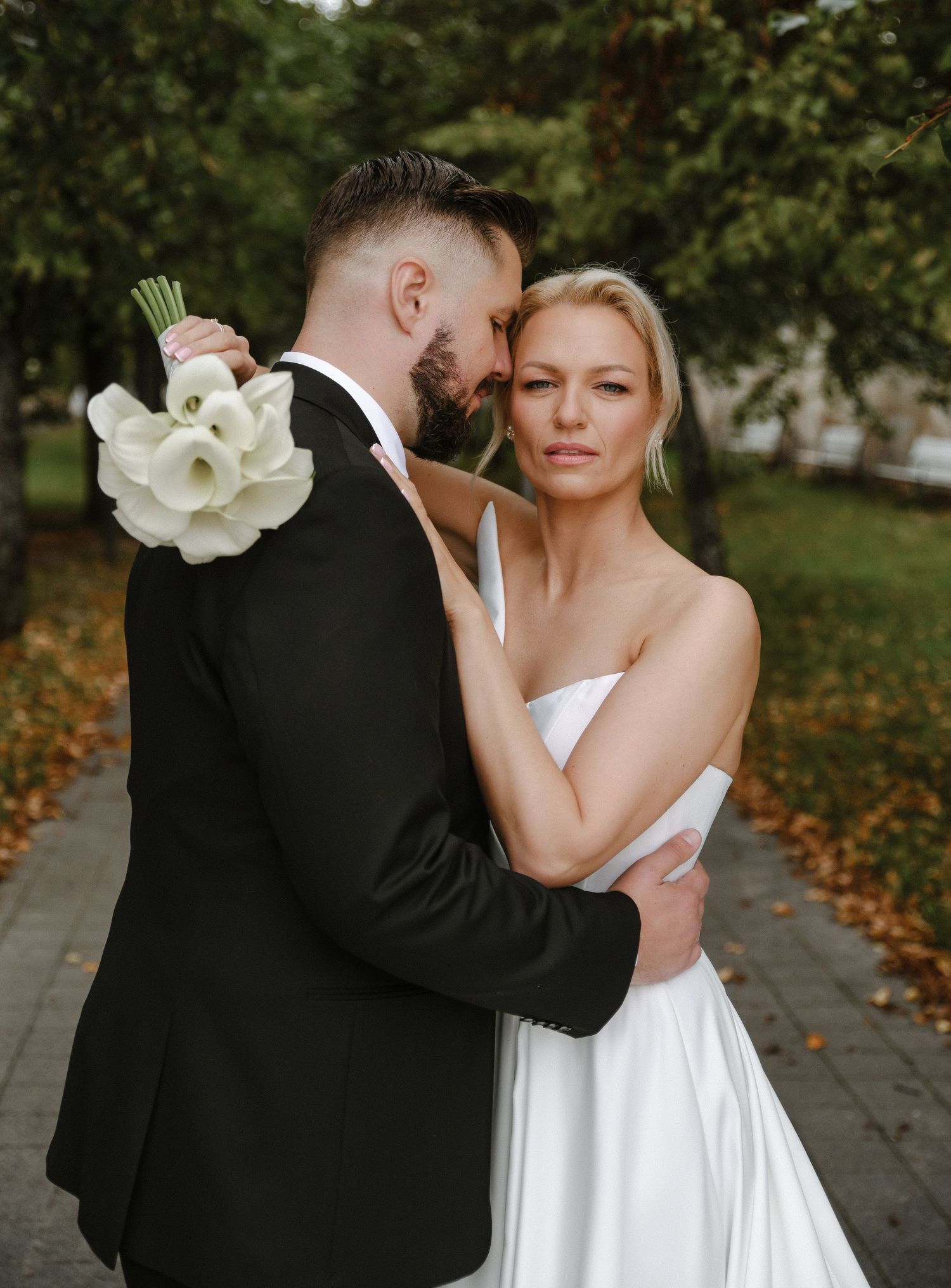 Wedding couple poses with calla lily bouquet in autumn outdoor setting.