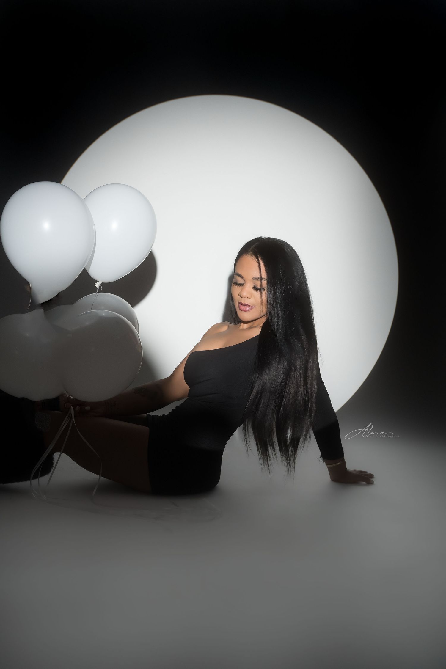 Dramatic studio portrait with white balloons and circular light backdrop.