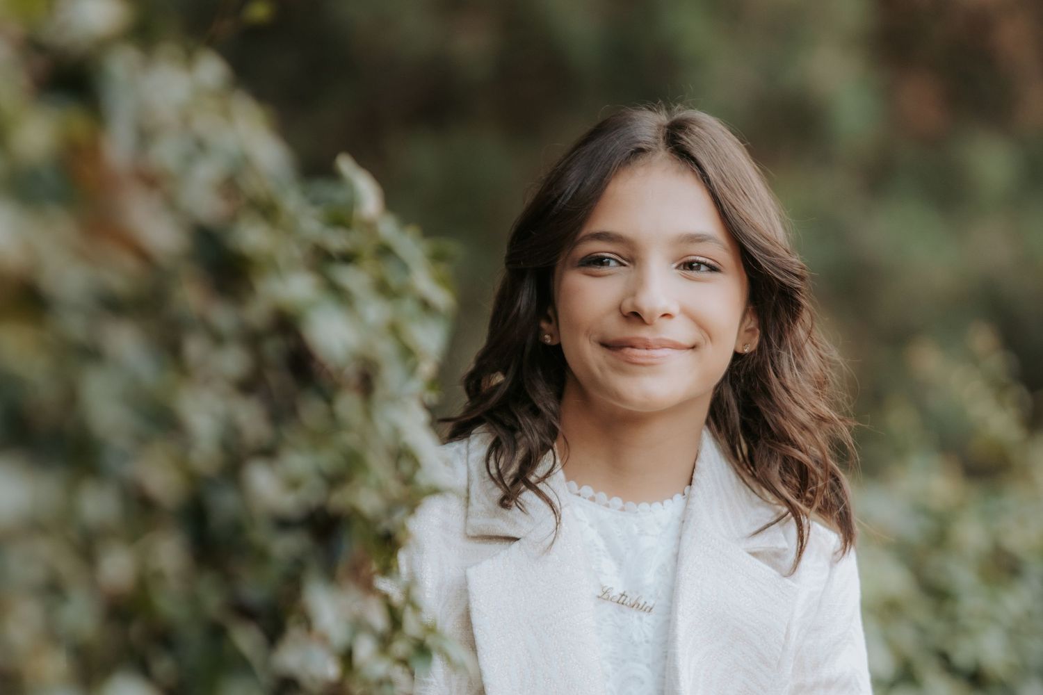 Woman in white dress poses outdoors against natural foliage backdrop in portrait photography session.