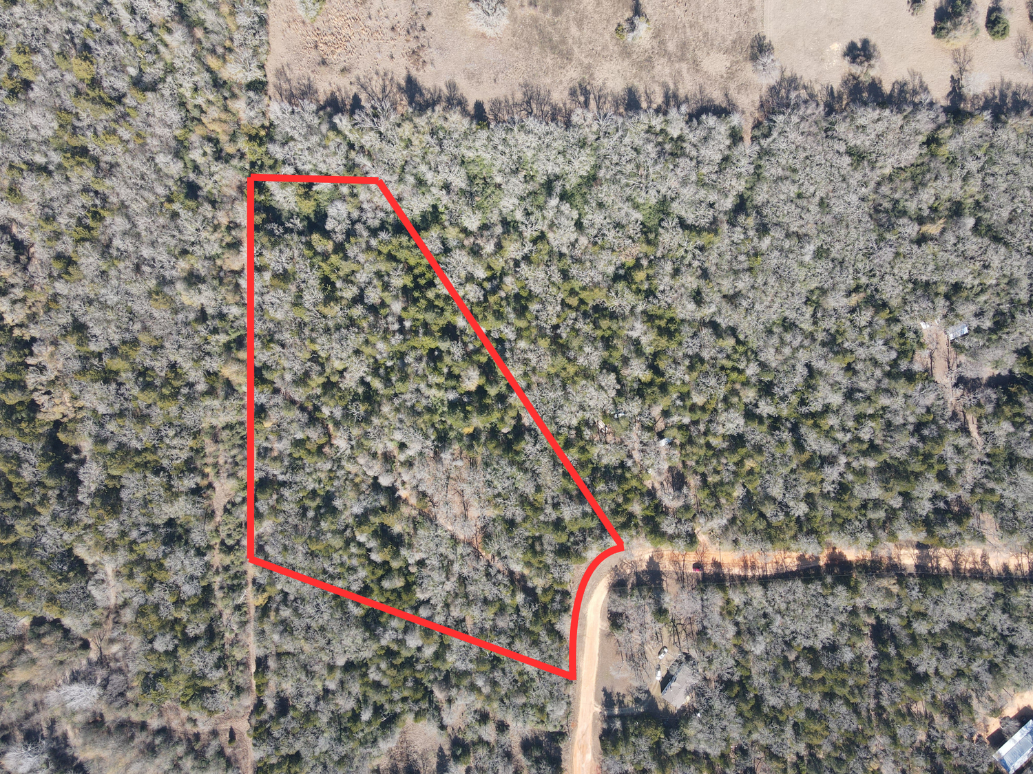 Aerial view of wooded property with a curved road and red boundary markers outlining an undeveloped parcel of land.
