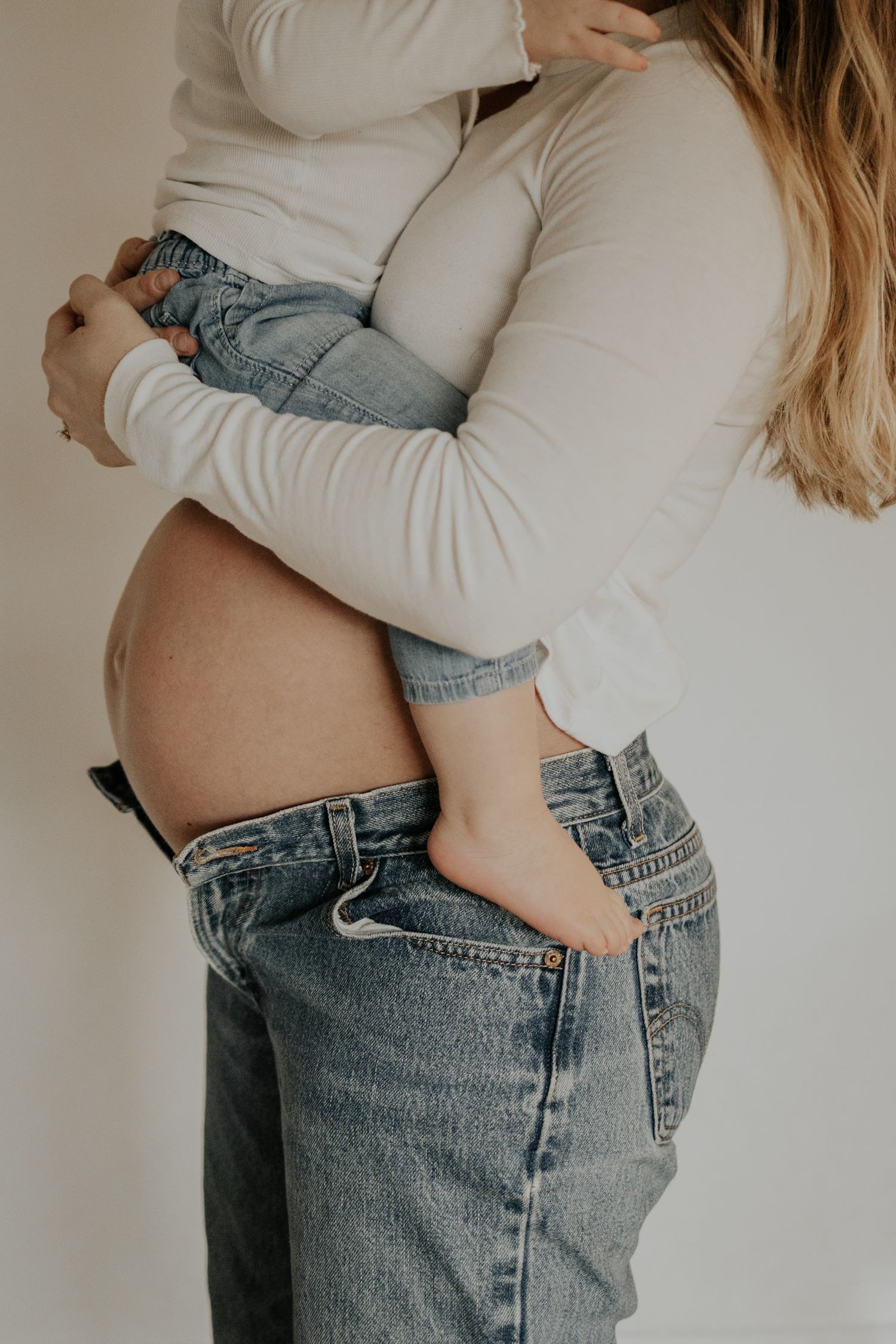 Cropped view of person in white sweater holding small child wearing blue jeans against white background.