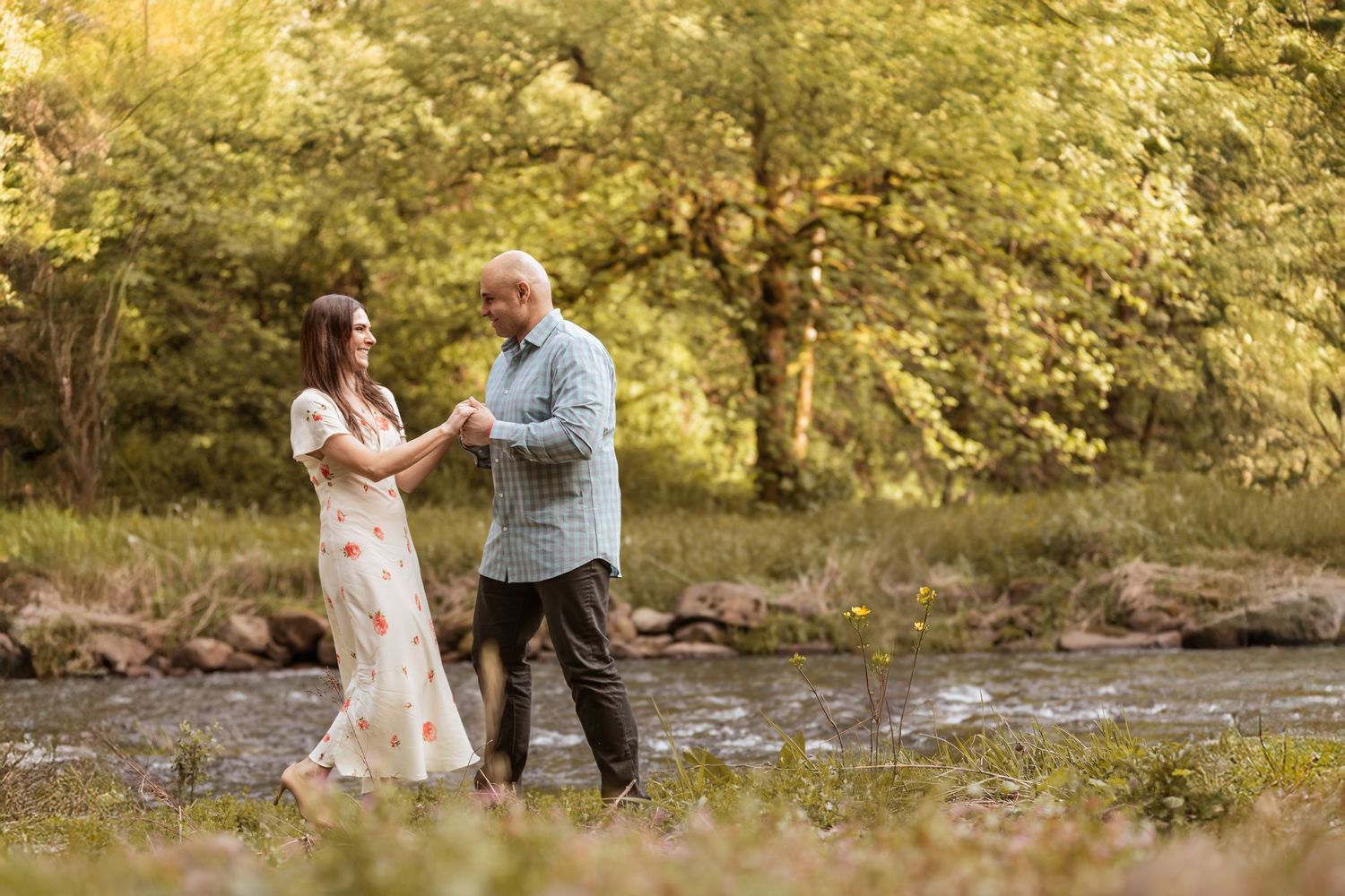 A couple dances together in a dreamy outdoor setting near a stream.