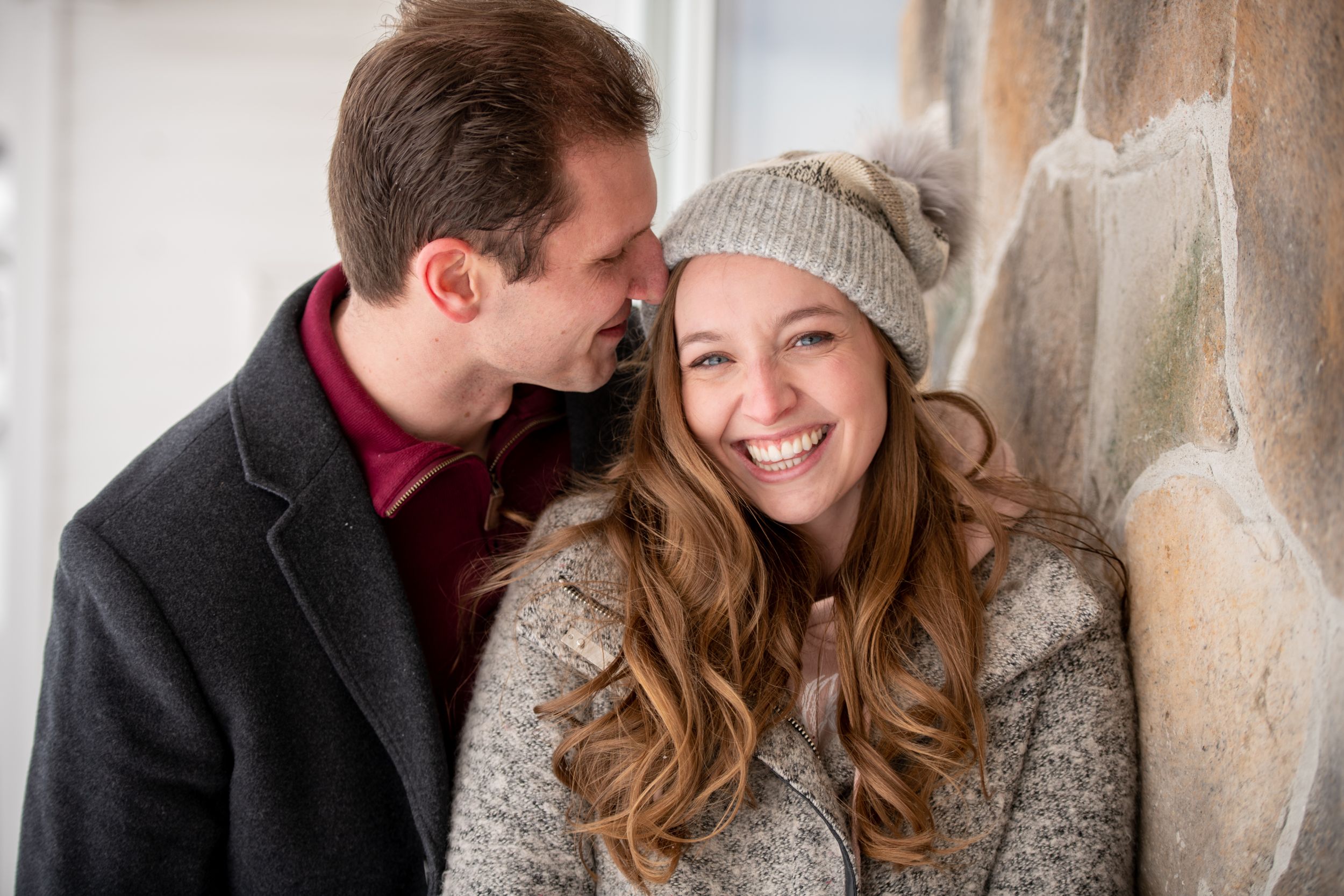 Winter engagement photos against a rustic stone wall backdrop.