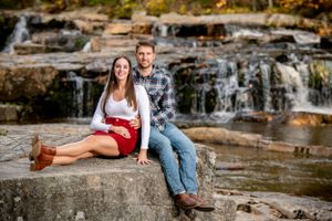 A couple poses casually on rocky waterfalls during an outdoor photo session.